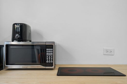A modern kitchen countertop with a microwave oven, a coffee maker, and an induction cooktop against a plain wall.