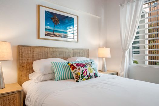 Your Personal Oasis: A cozy and bright bedroom awaits, complete with charming bedside lamps and a captivating palm tree print that brings the essence of a beach getaway indoors.