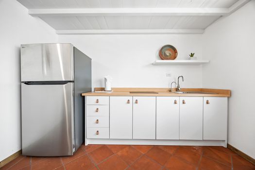 This efficient kitchenette features modern white cabinetry with sleek hardware, a practical countertop, and a full-sized stainless steel refrigerator. Perfect for convenient meal prep.