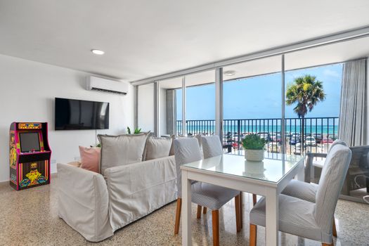 Spacious living room with L-shaped sofa, coffee table, arcade game, and open view to kitchen and dining area.