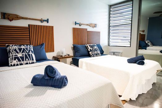 Perfect for friends or family, this comfortable room features two cozy beds, each with stylish wooden headboards and nautical-inspired decor.