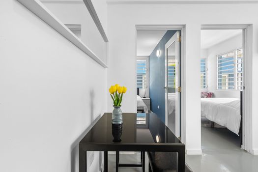 This contemporary room is stylish and comfortable, with ample lighting. The walls are painted white, giving off a clean and minimalist vibe. A black table is prominent at the forefront, holding a vase with yellow tulips.