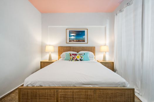 Dreamy Tropical Retreat: Unwind in our inviting bedroom featuring a comfortable bed with a stylish rattan headboard, flanked by warm, ambient lighting. The vibrant wall art adds a touch of paradise.