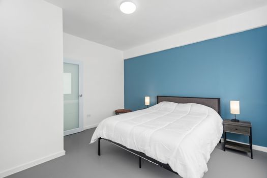 A serene space boasting a plush bed, minimalist decor, and a vibrant blue accent wall that adds a touch of warmth and sophistication.