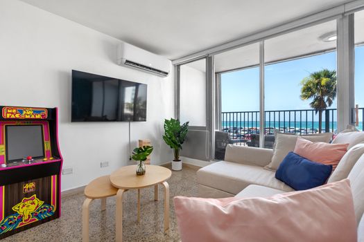 Bright living room with ocean view balcony, flat-screen TV, comfortable seating, and arcade game for entertainment.