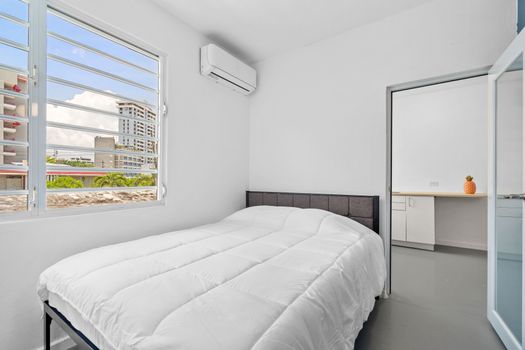 Experience urban living from this stylish bedroom featuring cityscape views, contemporary design, and a comfy bed to unwind. The large window allows ample natural light into the room, showcasing an urban view.
