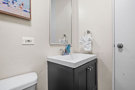 Enter our stylish and contemporary bathroom, boasting a chic dark vanity, complemented by a pristine white sink, and an elegant mirror.