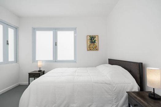La elegancia minimalista define este espacioso dormitorio, donde la luz natural entra a través de grandes ventanales que iluminan las impecables paredes y la cómoda ropa de cama.