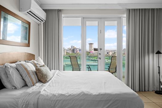 Relax and unwind in this serene bedroom, offering direct balcony access and an incredible panorama of the lagoon and cityscape. Enjoy the natural light and the gentle breeze, creating a peaceful sanctuary for your escape.