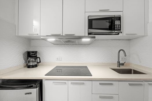 Whip up delicious meals in your fully equipped, modern kitchen featuring sleek white cabinetry, a microwave, and a convenient cooktop. Perfect for preparing your morning coffee or a gourmet dinner!