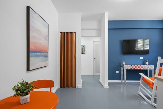 A modern, colorful room with a blue accent wall, white rocking chairs, and a flat-screen TV, showcasing a world map and abstract art on the walls, creating a lively and comfortable space.