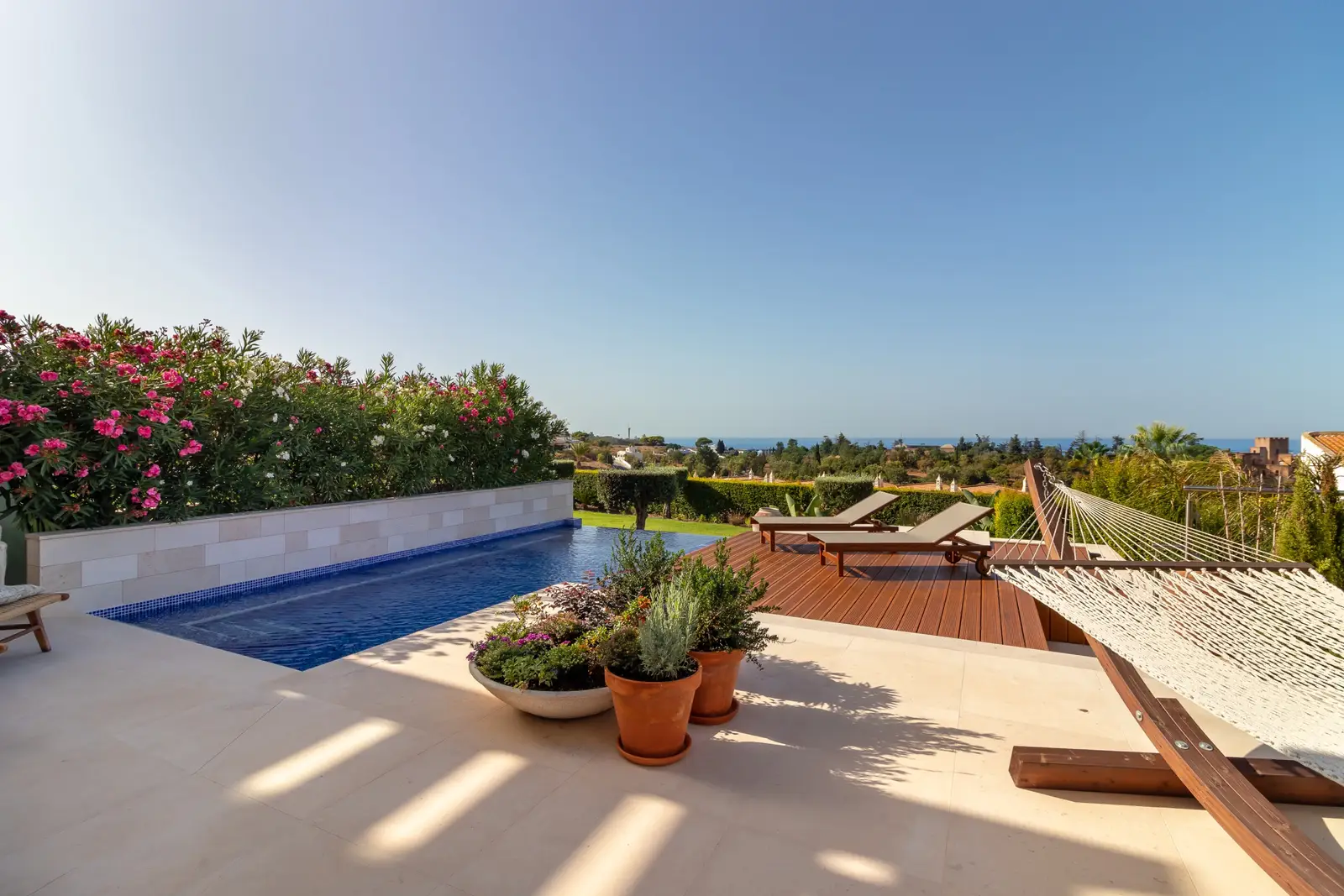 Infinity pool, wooden sun deck with loungers and hammock, potted herbs in the foreground