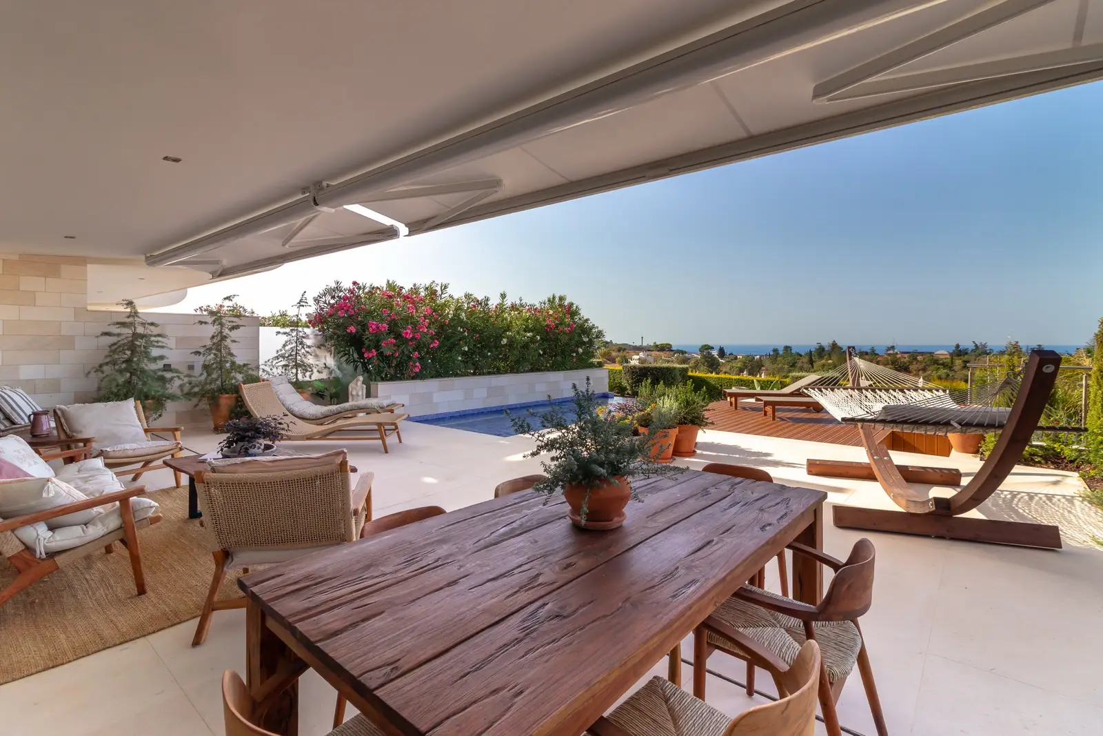 Covered terrace with a long wooden dining table, lounge seating and the pool beyond