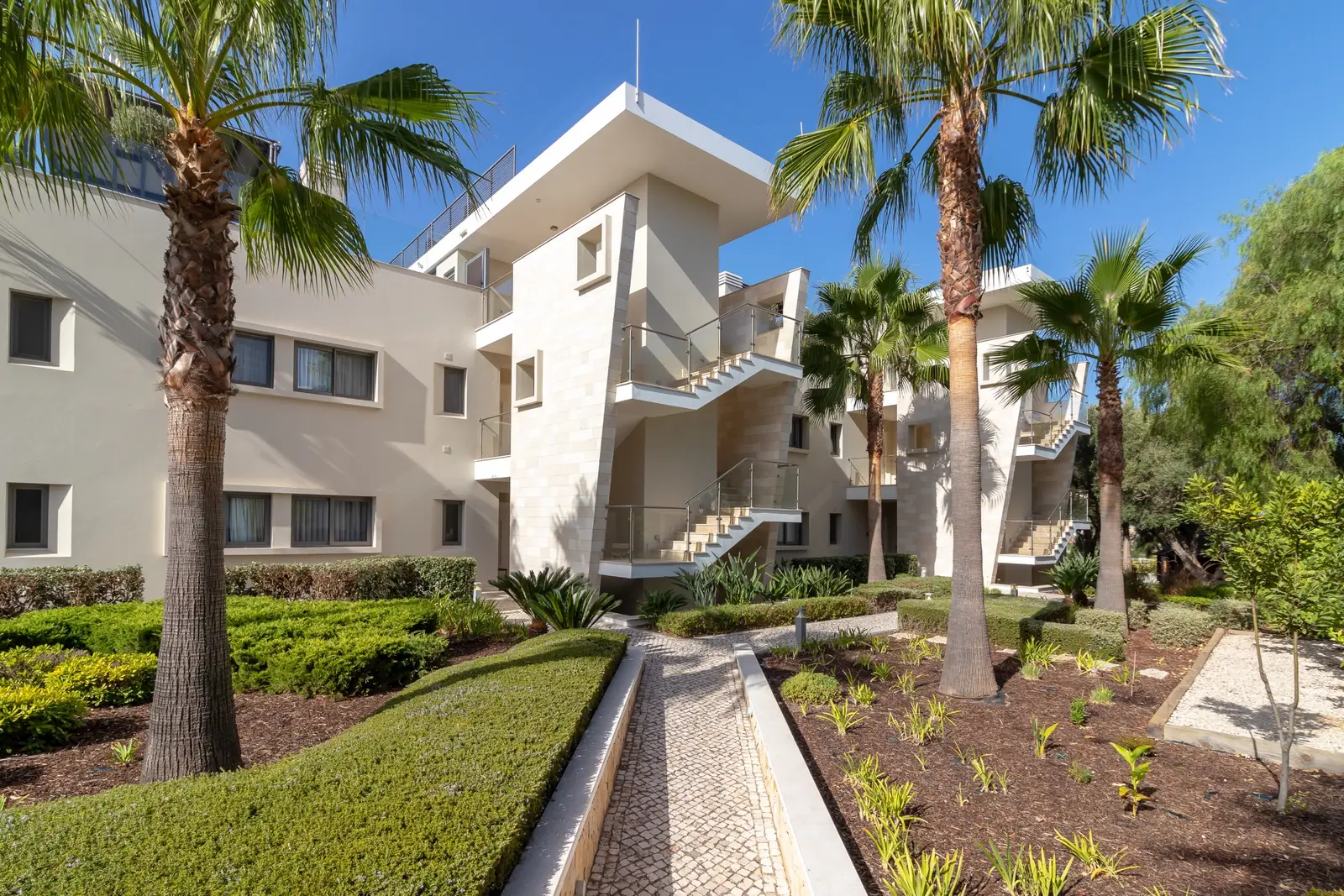 White contemporary apartment building with external stairs set among palm trees and clipped hedges