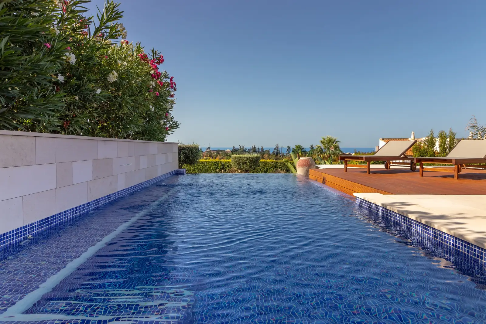 Mosaic-tiled infinity pool edge with the wooden deck and the sea on the horizon