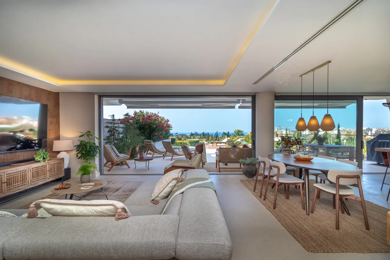 Open-plan living room with sliding glass panels fully open to the terrace loungers and sea view