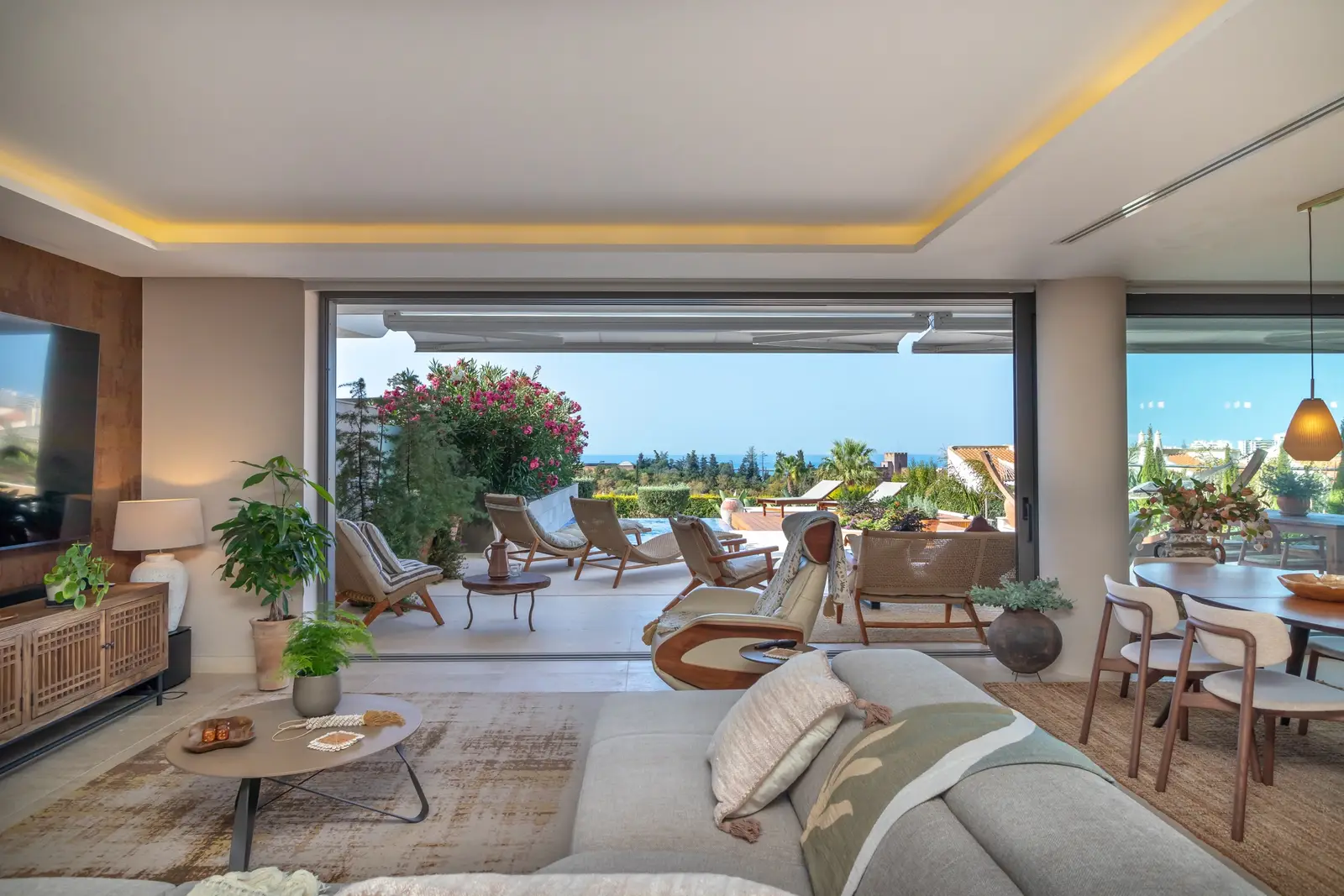Living room sofa and dining table with the terrace and sea view through open glass panels