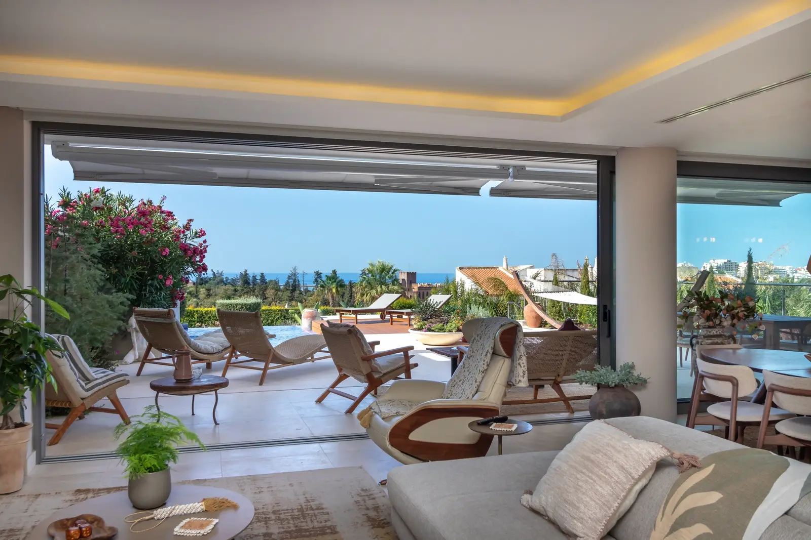 Living room looking through the open glass wall to the terrace, loungers and pool
