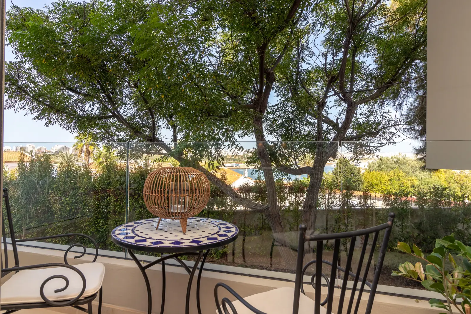 Balcony bistro table with mosaic top and wrought iron chairs under mature trees