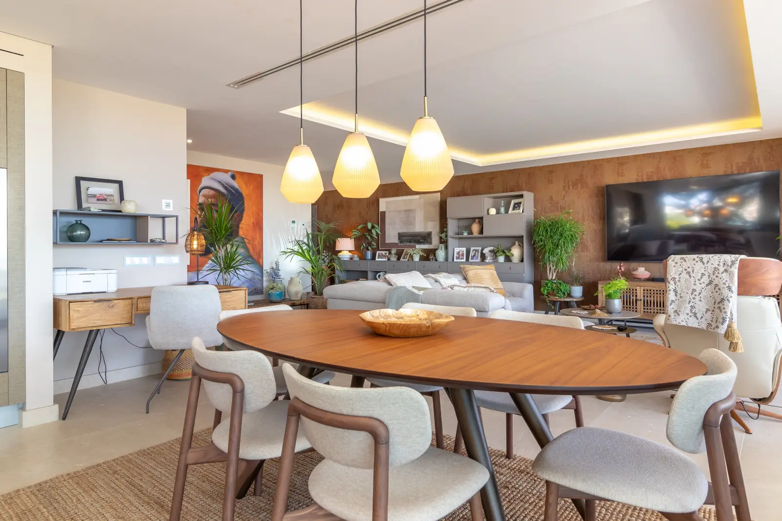Dining table for six under rattan pendant lights with a writing desk and living area behind