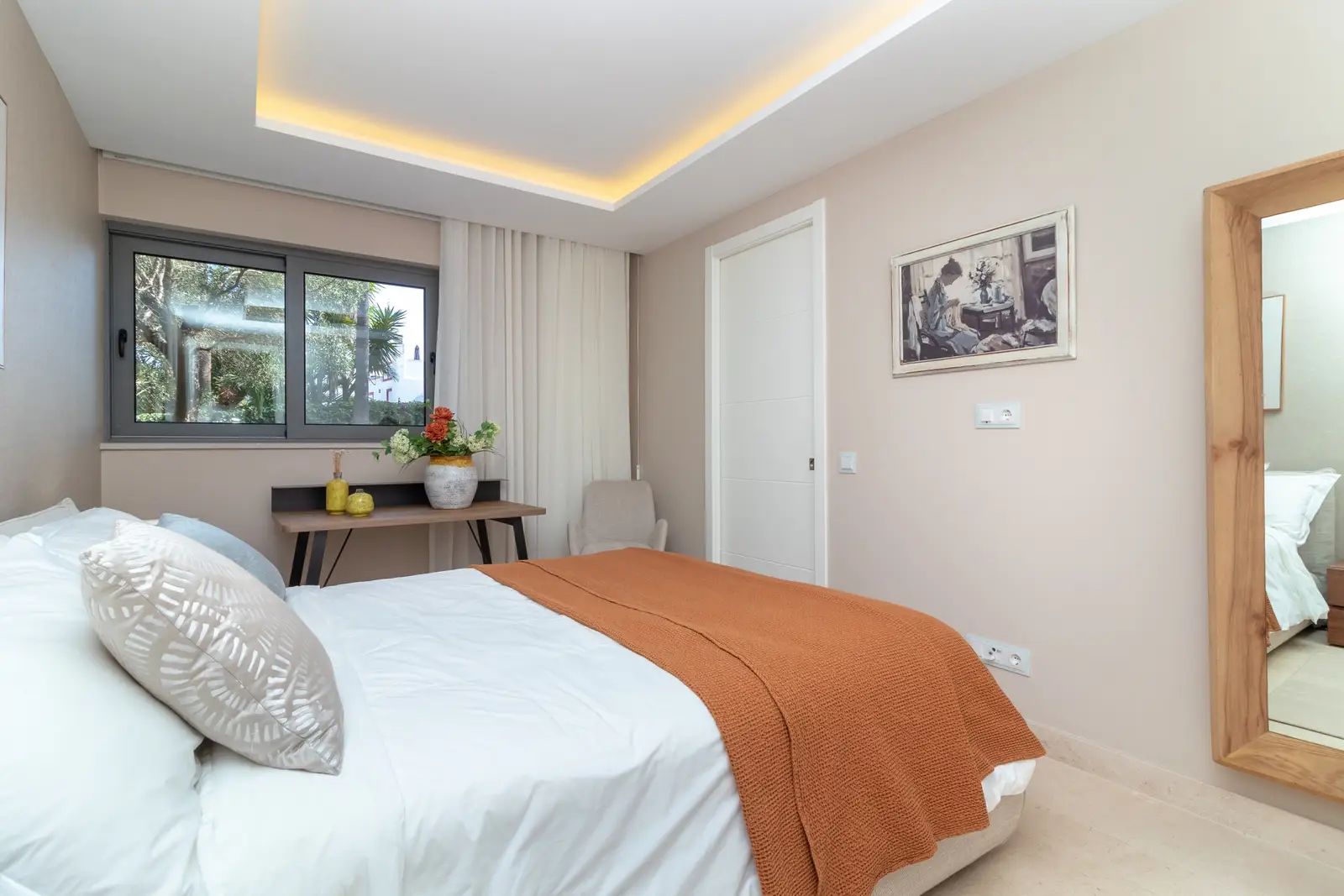 Bedroom with double bed, orange throw, desk and full-length mirror, window onto the garden