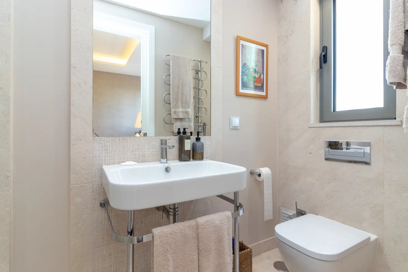 En-suite bathroom with wall-hung basin, towel rail, framed print and window
