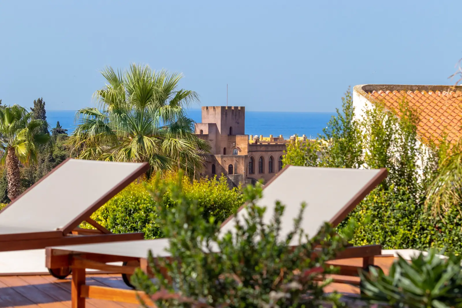 Two white sun loungers on the wooden deck facing the castle and the sea