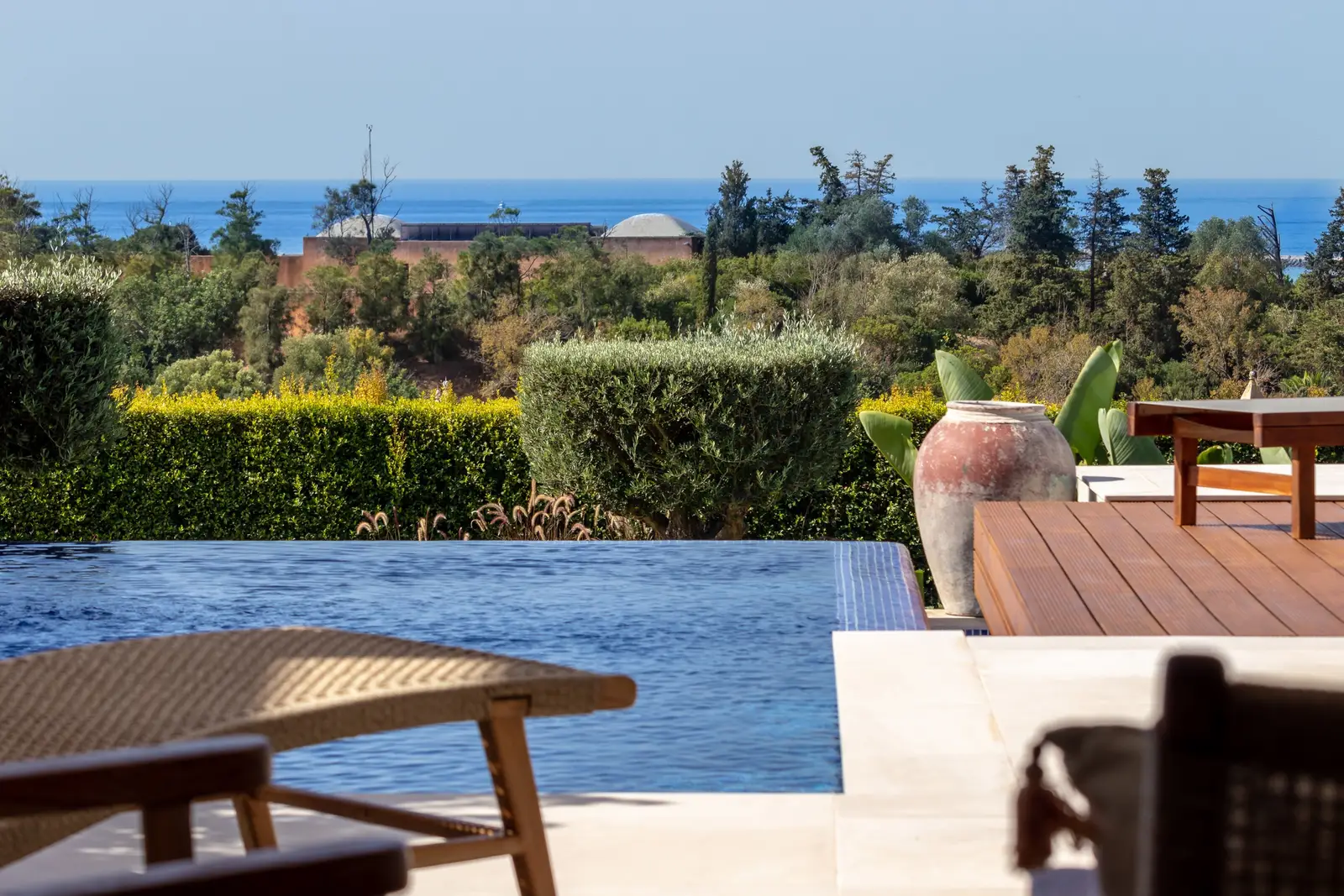 Infinity pool edge with hedges and trees below and the sea on the horizon