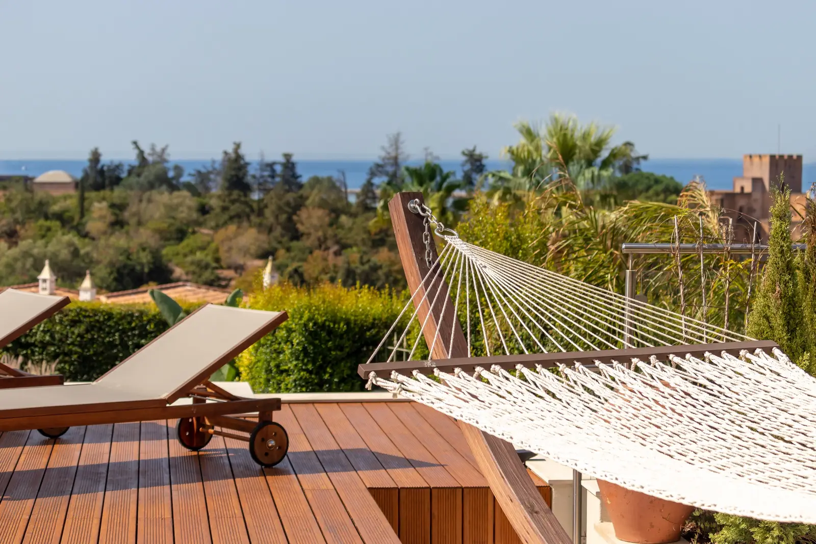 Rope hammock on the wooden sun deck with sea view and loungers behind