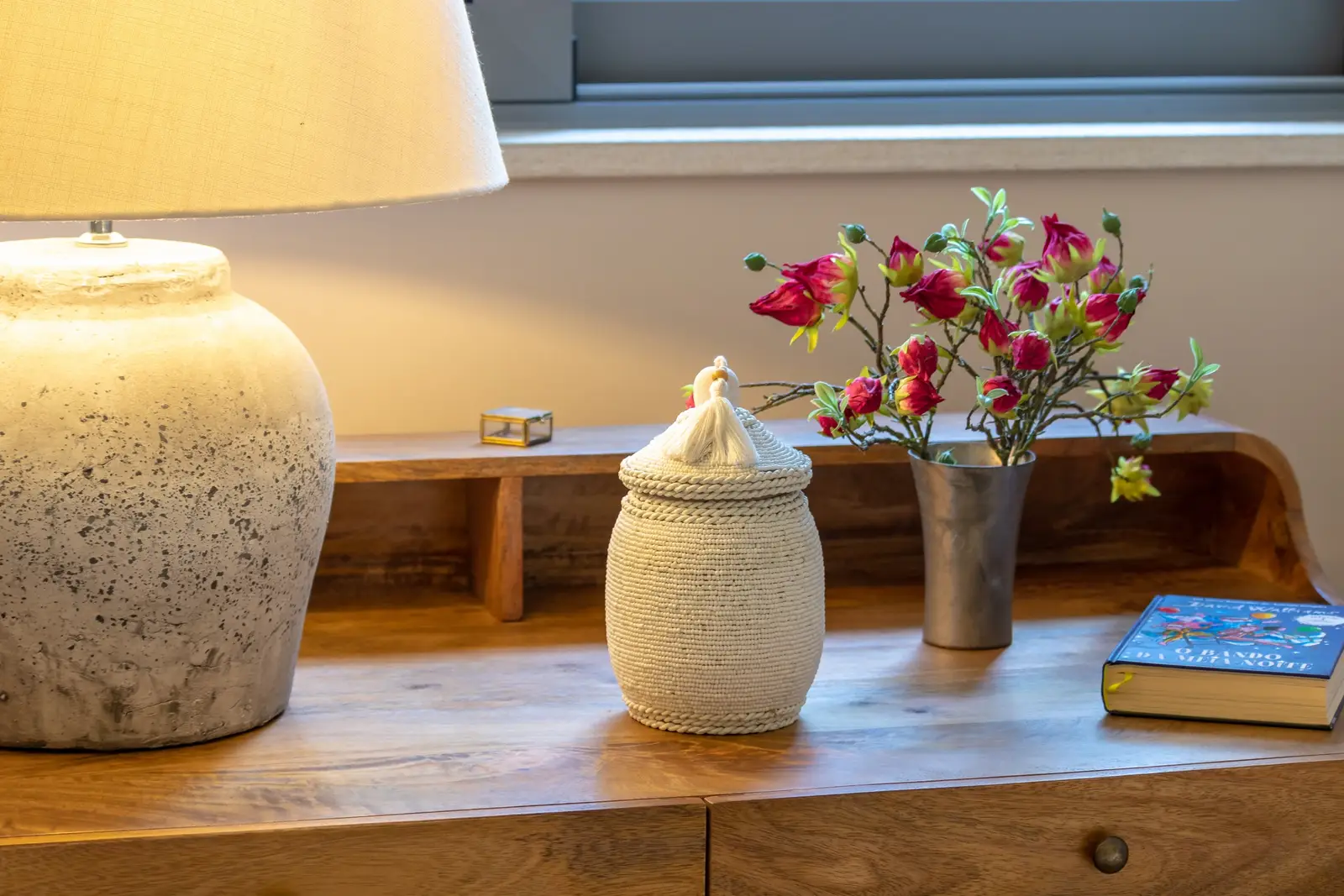 Dressing table with stone lamp, woven jar and flowers beside the window