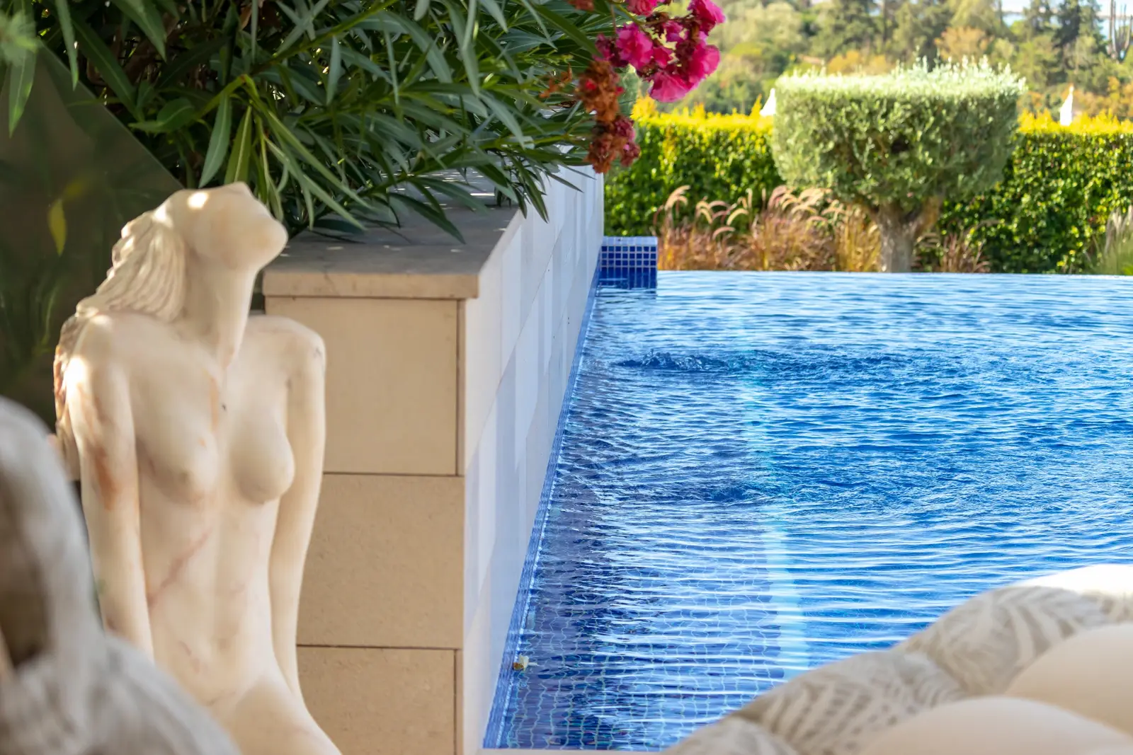 Stone figure sculpture beside the mosaic-tiled infinity pool and oleander