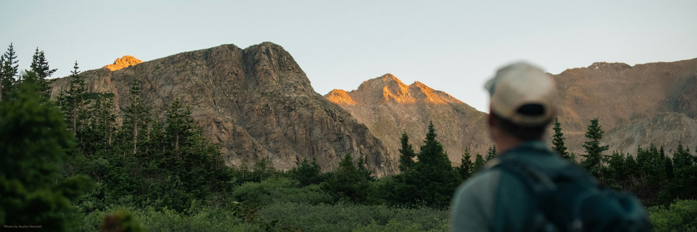 Hiker looking at snow-capped Rocky Mountain peaks during Colorado spring mud season.