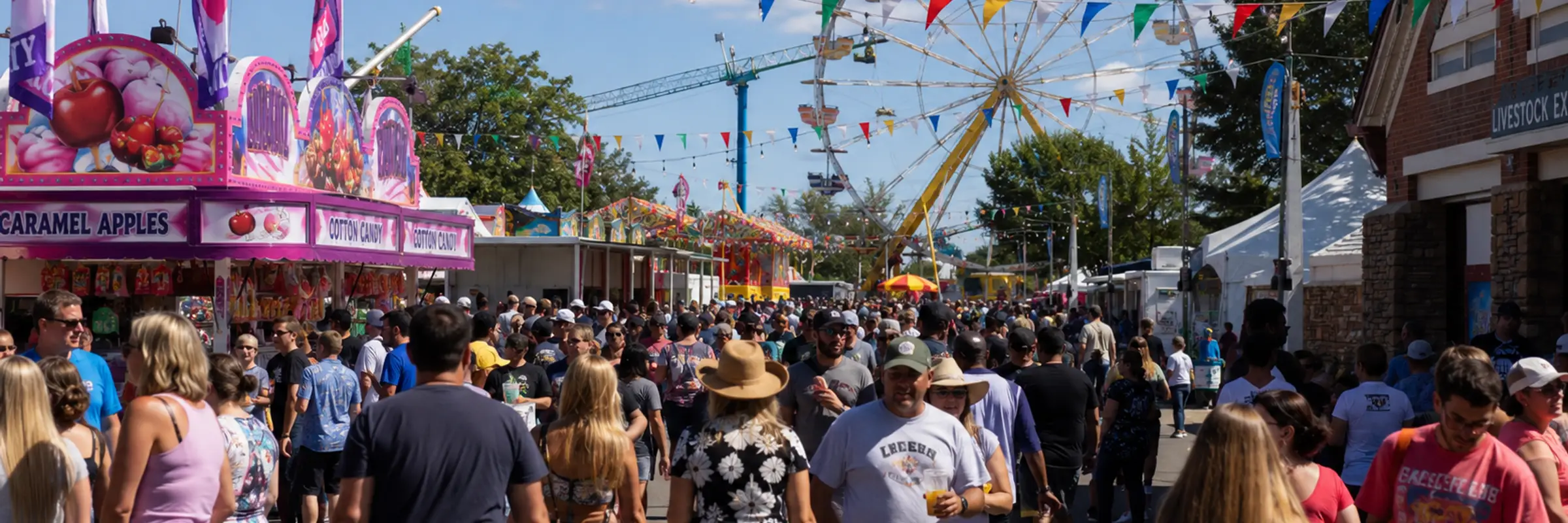 Crowded daytime view of the Colorado State Fair midway with colorful decorations, food vendors, carnival rides, and visitors walking through the fairgrounds.