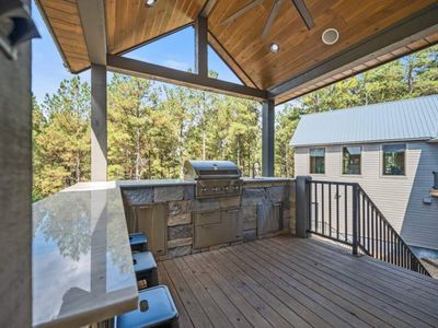 Outdoor kitchen with gas grill, bar top seating and mini fridge.