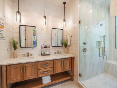 This bath comes with a spacious double-sink vanity with warm wood tones, crisp white countertops, and whitewashed wood walls—elegance and functionality meet in perfect harmony.