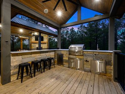 Outdoor kitchen with gas grill, bar top seating and mini fridge.