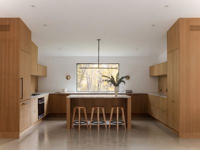 Chef's kitchen in white oak with a stone island, counter seating, and a forest view.