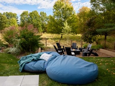 Oversized loungers on the pool deck with propane fire pit in the background and meadow beyond.