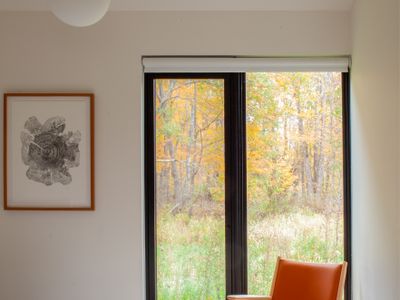 Serene bedroom with a leather lounge chair framing the meadow beyond.