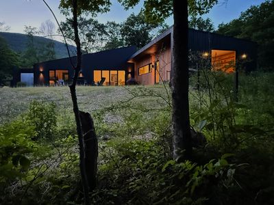 As evening falls, The Heron House glows against the meadow and the Catskills beyond.