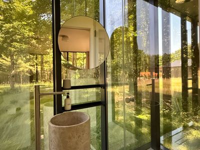 Glass-walled shower and stone vanity, open to the forest just beyond the pane.