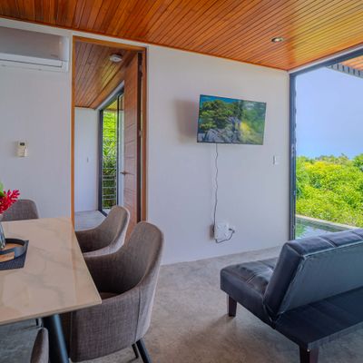 Bright living and dining area with TV, terrace access, and tropical views.