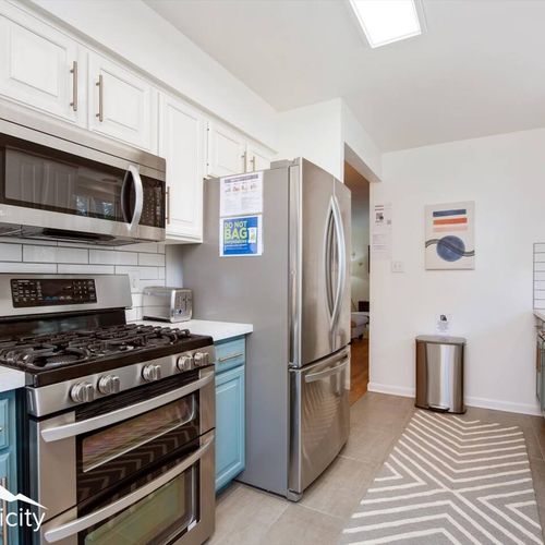 - modern appliances including gas stove, microwave, and spacious fridge
- chevron pattern rug adds flair while tile floors keep cleanup easy
- crisp white cabinetry with gold pulls ties the look together effortlessly