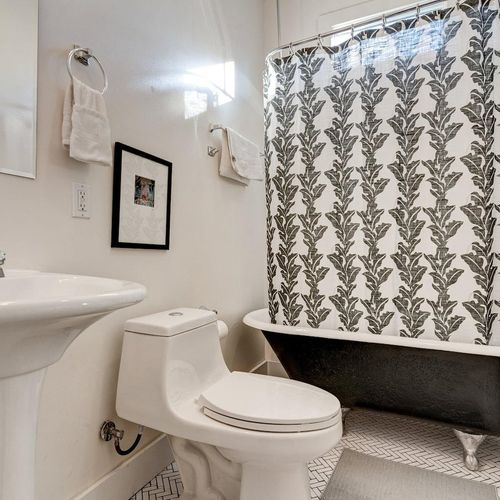 Charming bathroom w/ a clawfoot tub, bold printed curtain & pedestal sink.