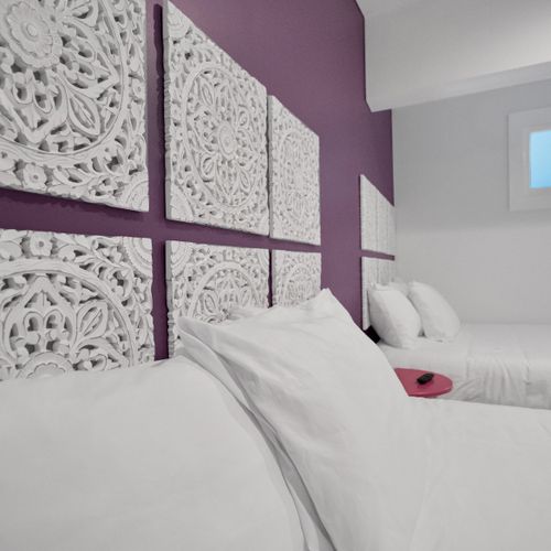Bedroom 2 w/ a bold purple headboard wall & crisp white linens for a dramatic retreat.