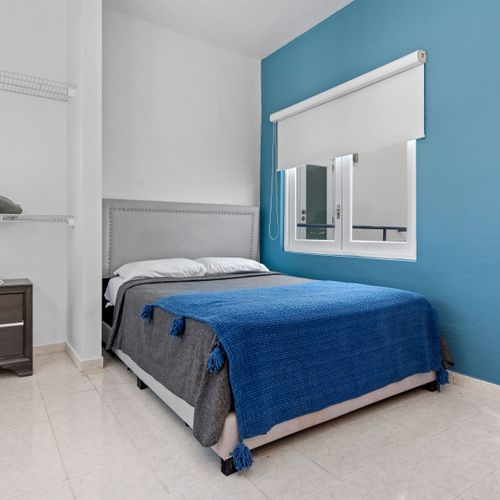 Relax in a peaceful bedroom featuring a comfortable bed paired with a vibrant blue blanket that contrasts beautifully with the calm blue accent wall.