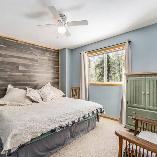 Peaceful bedroom with a plush king bed, wood accent wall, and forest views