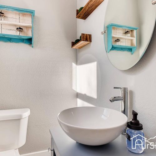 - sleek modern bathroom with vessel sink, oval mirror, and clean modern lines throughout
- wooden accent shelves and blue vintage boxes offer functional charm
- bright natural light makes this compact vanity space feel open and fresh
