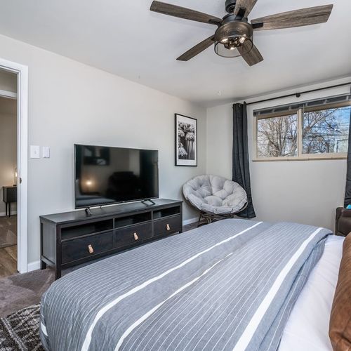 - primary bedroom features a flat screen tv cozy papasan chair and soft linens
- large windows bring in natural light while blackout curtains offer privacy
- relax watch a movie or read in comfort in this spacious well lit retreat