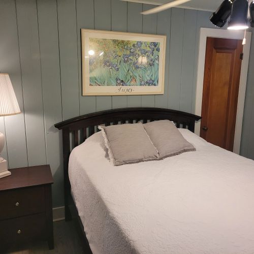 Bedroom #5 (beach house, main floor):  private bedroom with a queen-size bed, ceiling fan, dresser, nightstand, lamp, mirror, and a travel crib.